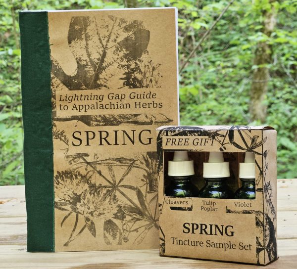 A booklet with a brown cover and green spine labeled "Lighting Gap Guide To Appalachian Herbs: SPRING", next to a small box with three green dropper bottles inside. The box says "FREE GIFT: SPRING Tincture Sample Set".